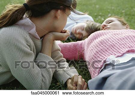 Girl contemplatively observing mother and brother reclining, resting on grass View Large Photo Image Stock Image - Girl contemplatively observing mother and brother reclining, resting on grass. Fotosearch