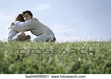Stock Image - Girl embracing her younger brother in grassy field. Fotosearch