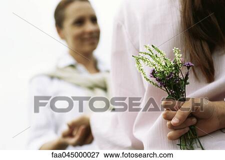 Stock Photo - Girl hiding wildflower bouquet behind back, holding mother's hand, cropped. Fotosearch