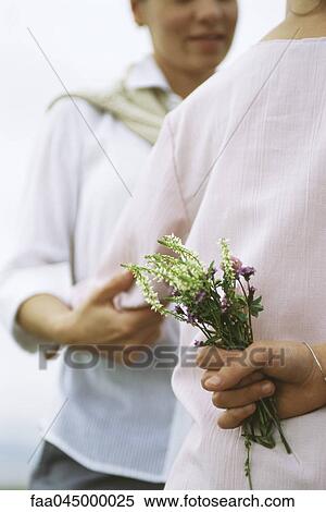 Stock Photography - Girl holding wildflower bouquet behind back, embracing mother. Fotosearch