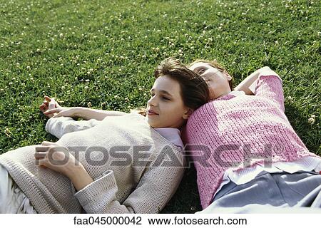 Stock Image - Girl reclining on grass with mother, daydreaming. Fotosearch