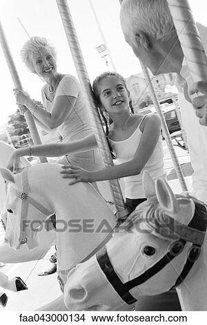 Girl riding carousel with her grandparents View Large Photo Image Picture - Girl riding carousel with her grandparents. Fotosearch