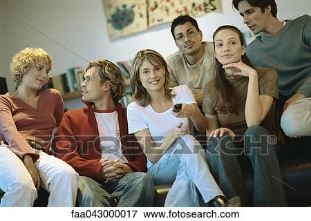 Stock Photo - Group of friends sitting close together on sofa watching TV. Fotosearch