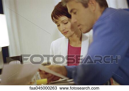 Stock Image - Man and woman sitting at table reading documents. Fotosearch