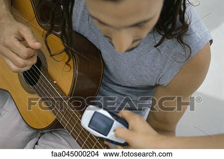 Man playing acoustic guitar, person showing cell phone View Large Photo Image Picture - Man playing acoustic guitar, person showing cell phone. Fotosearch