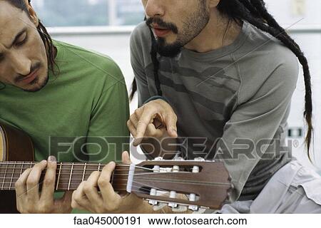 Stock Image - Man teaching friend to play acoustic guitar. Fotosearch