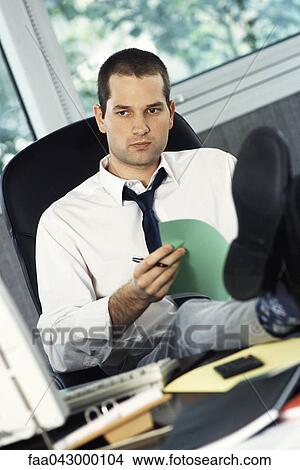 Man with feet up on office desk holding document, looking away View Large Photo Image Picture - Man with feet up on office desk holding document, looking away. Fotosearch