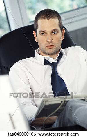 Stock Photography - Man with feet up on office desk, typing on computer keyboard set on lap. Fotosearch