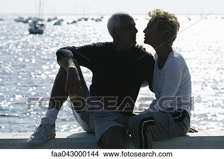 Mature couple sitting together on pier, backlit View Large Photo Image Picture - Mature couple sitting together on pier, backlit. Fotosearch