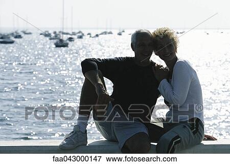 Mature couple sitting together on pier, backlit View Large Photo Image Stock Photo - Mature couple sitting together on pier, backlit. Fotosearch