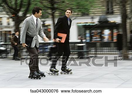 Stock Photograph - Men in business attire inline skating together along sidewalk carrying briefcase, folders under arm. Fotosearch