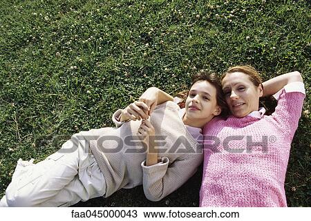 Stock Image - Mother and daughter lying together on grass, smiling at camera. Fotosearch