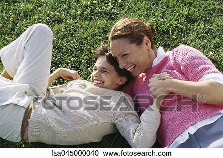 Stock Image - Mother and daughter reclining in grass, laughing, holding hands. Fotosearch