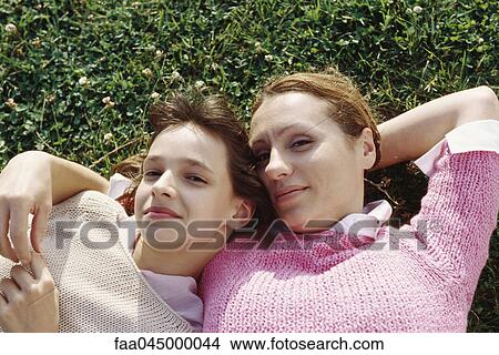 Mother and daughter reclining on grass together, smiling at camera View Large Photo Image Picture - Mother and daughter reclining on grass together, smiling at camera. Fotosearch