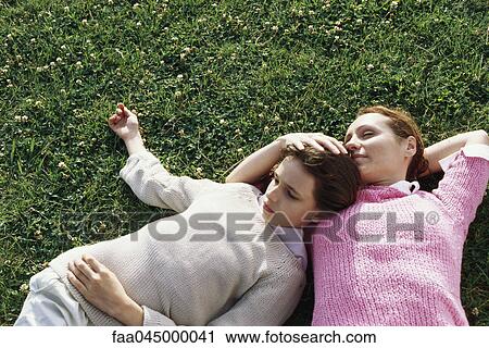 Stock Image - Mother and daughter reclining together in grass. Fotosearch