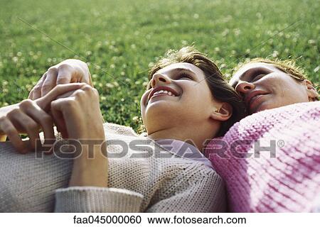 Stock Image - Mother and daughter reclining together on grass, girl resting head on mother's shoulder. Fotosearch