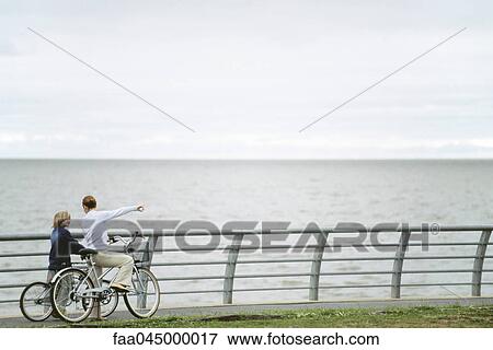 Stock Photo - Mother and son on bicycle outing at seaside park, mother pointing to distance. Fotosearch
