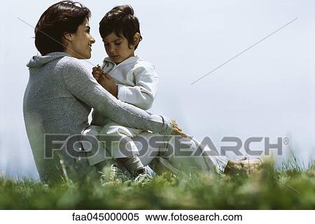Stock Photography - Mother sitting in grass with young son on lap. Fotosearch