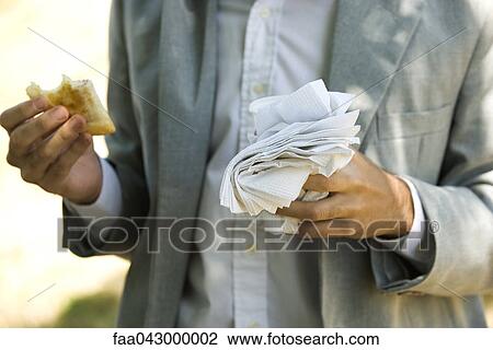 Stock Image - Person holding half eaten pastry in one hand and disposable cup and paper napkins in other hand. Fotosearch