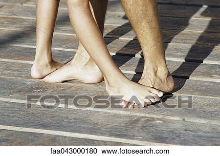 Stock Image - Person standing on top of another person's bare feet, cropped. Fotosearch