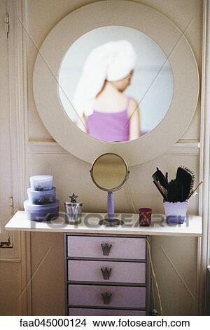 Picture - Reflection of woman with head wrapped in towel in mirror hanging above woman's dressing table. Fotosearch