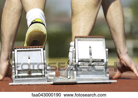 Stock Image - Runner crouching on starting blocks, cropped rear view. Fotosearch