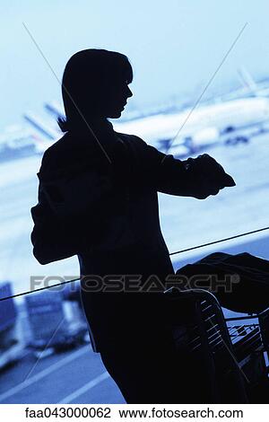 Stock Image - Silhouette of woman traveler looking at watch in airport. Fotosearch