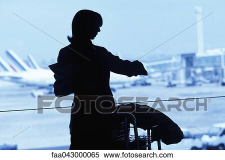 Stock Photography - Silhouette of woman traveler looking at watch in airport. Fotosearch