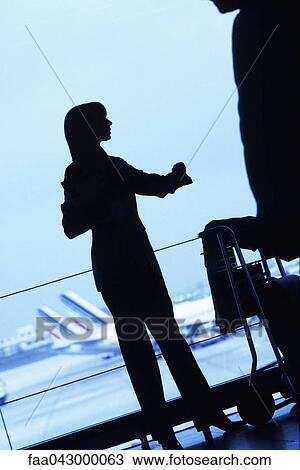 Silhouette of woman traveler standing with luggage cart looking away in airport View Large Photo Image Stock Image - Silhouette of woman traveler standing with luggage cart looking away in airport. Fotosearch