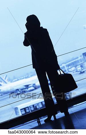 Silhouette of woman traveler using cell phone, holding travel bag in airport View Large Photo Image Picture - Silhouette of woman traveler using cell phone, holding travel bag in airport. Fotosearch
