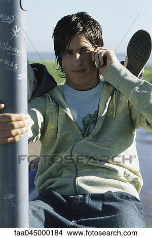 Teenage boy using cell phone, friend's feet resting on his shoulders View Large Photo Image Picture - Teenage boy using cell phone, friend's feet resting on his shoulders. Fotosearch