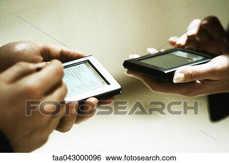 Stock Photograph - Two people exchanging information using personal digital assistants. Fotosearch