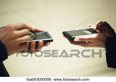 Stock Photography - Two people exchanging information using personal digital assistants. Fotosearch