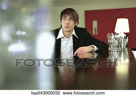 Stock Image - Well dressed young man leaning on bar, looking away. Fotosearch