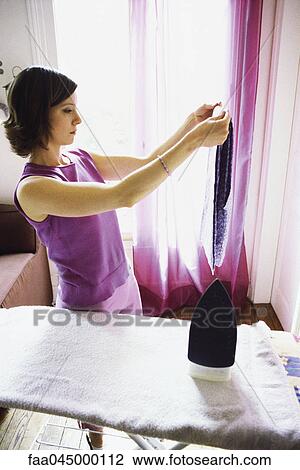Stock Image - Woman doing ironing, holding up blouse. Fotosearch