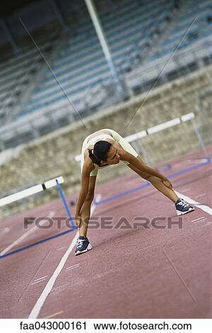 Stock Image - Woman doing stretches on running track. Fotosearch