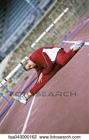 Stock Image - Woman doing stretches on running track. Fotosearch