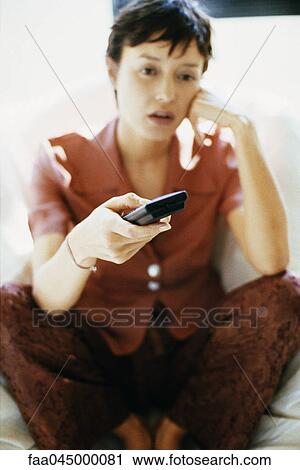 Stock Image - Woman holding remote control, dull expression on face. Fotosearch