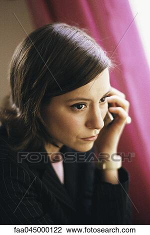 Stock Image - Woman listening to phone call, looking away pensively. Fotosearch