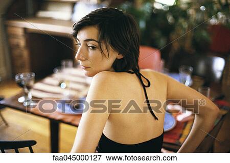 Stock Photo - Woman looking over shoulder contemplatively looking away, set table in background. Fotosearch