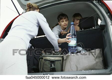 Stock Image - Woman organizing luggage in back of car, children looking over back seat. Fotosearch