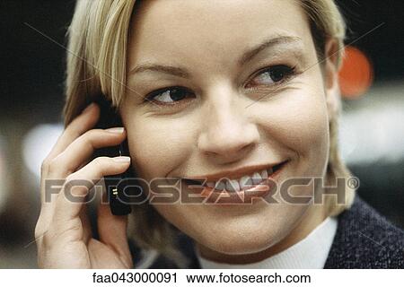 Stock Image - Woman phoning using cell phone smiling, glancing sideways, portrait. Fotosearch