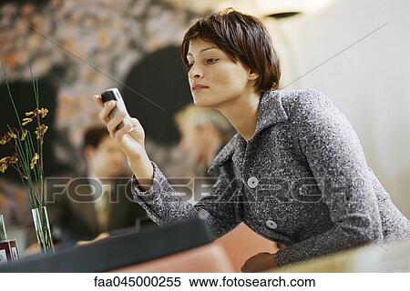 Stock Photography - Woman sitting alone in restaurant, looking at cell phone. Fotosearch