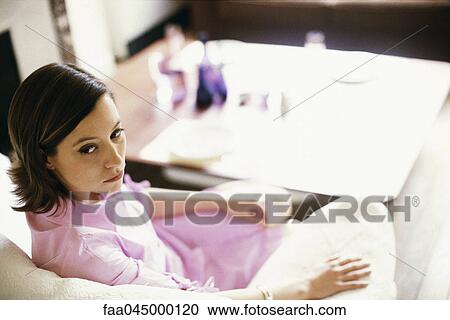Stock Image - Woman sitting on sofa looking over shoulder. Fotosearch