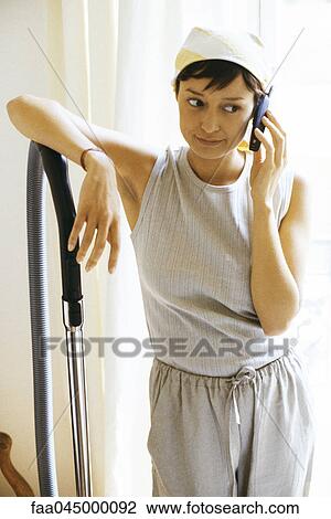 Stock Image - Woman taking break from housework for phone call, looking away. Fotosearch