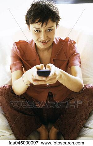 Stock Photo - Woman watching TV, changing channel. Fotosearch