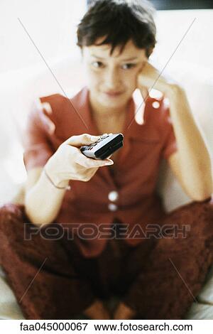 Stock Photo - Woman watching TV, changing channels. Fotosearch