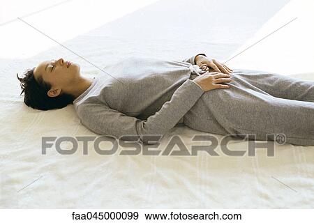 Stock Photo - Woman wearing athletic wear lying on back with hands placed on lower abdomen. Fotosearch