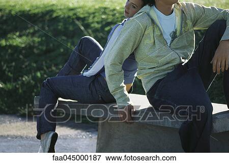 Stock Photo - Young couple sitting back to back on park bench. Fotosearch
