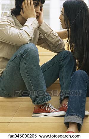 Stock Photography - Young couple together on steps, man holding head, woman consoling. Fotosearch